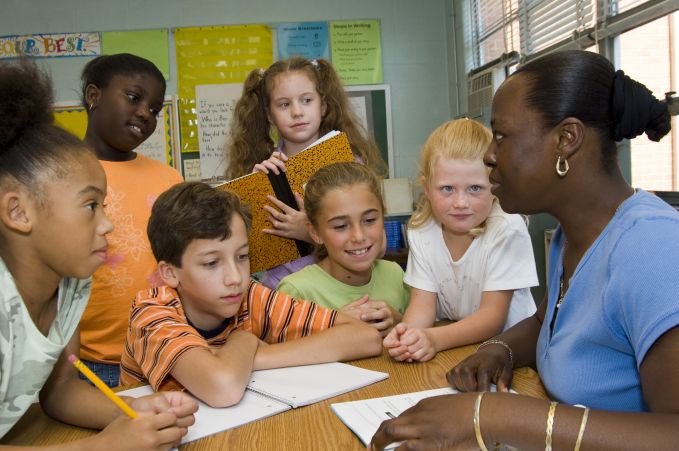Black woman surrounded by diverse students in a classroom.