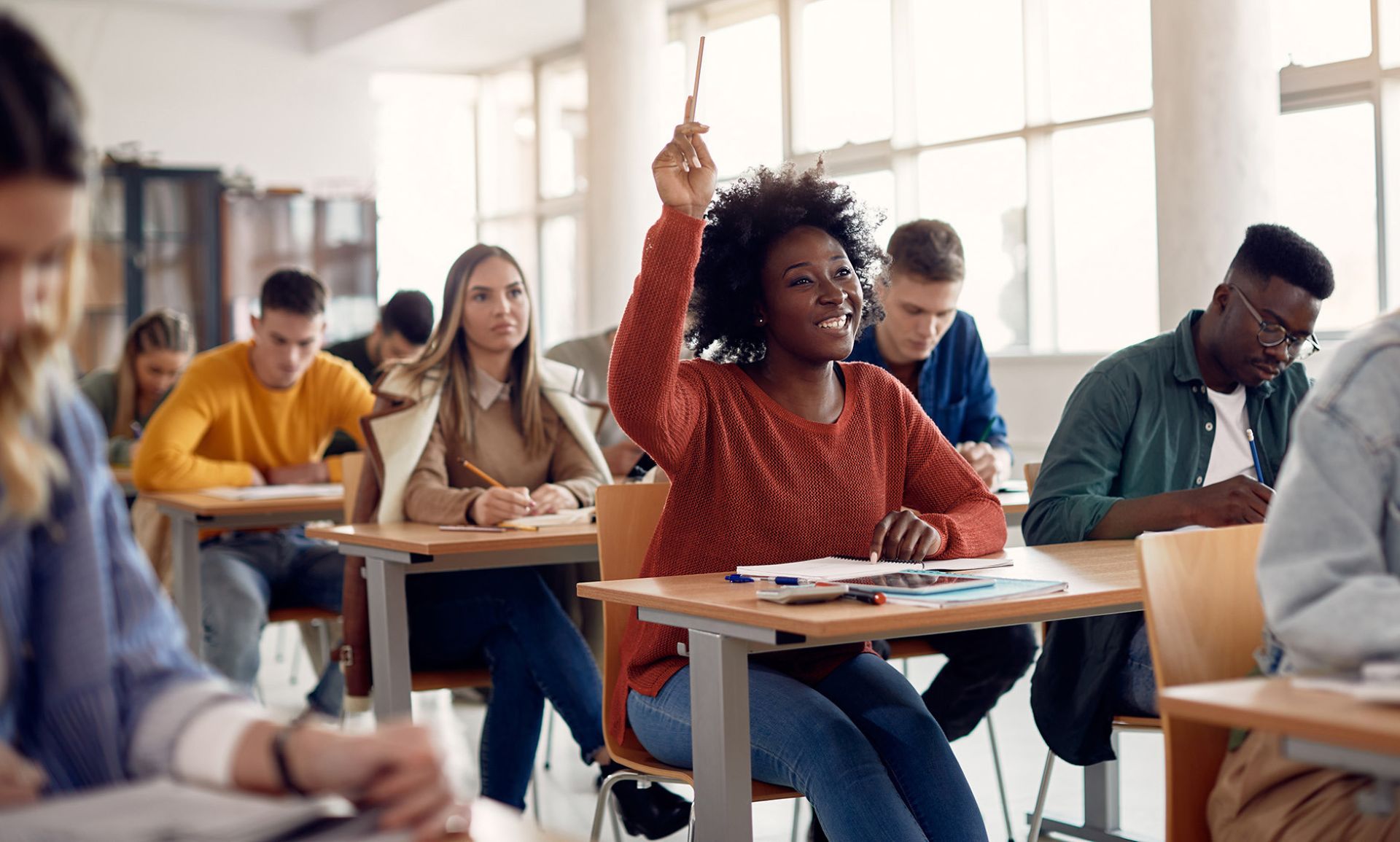 Black female student with hand raised in high school classroom.