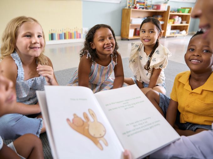 Diverse kindergarteners on a classroom carpet listening to a story.