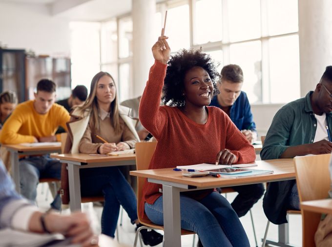 Black female student with hand raised in high school classroom.