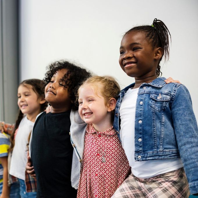 Young black, white, and brown students with arms around each other in a classroom.