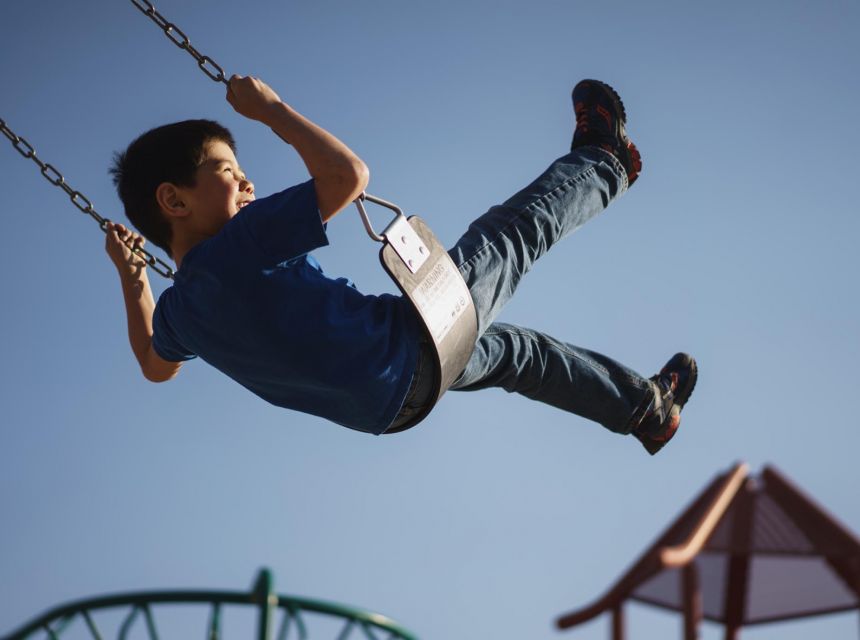 Smiling brown-skinned boy on a swing under a blue sky.