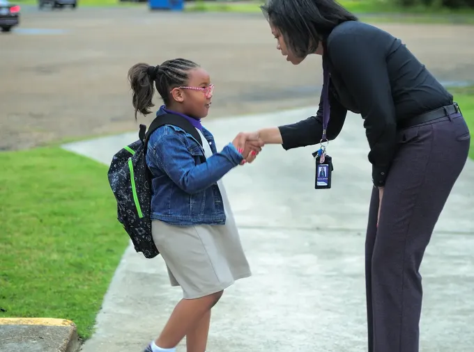 Director greets student entering school.