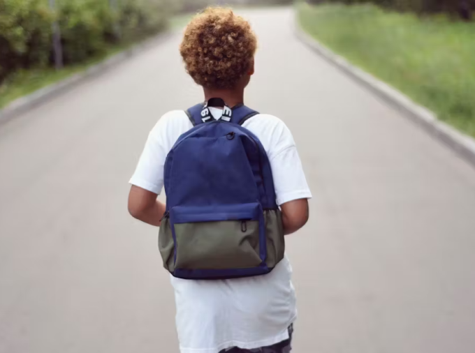 Black boy with backpack walking down road.